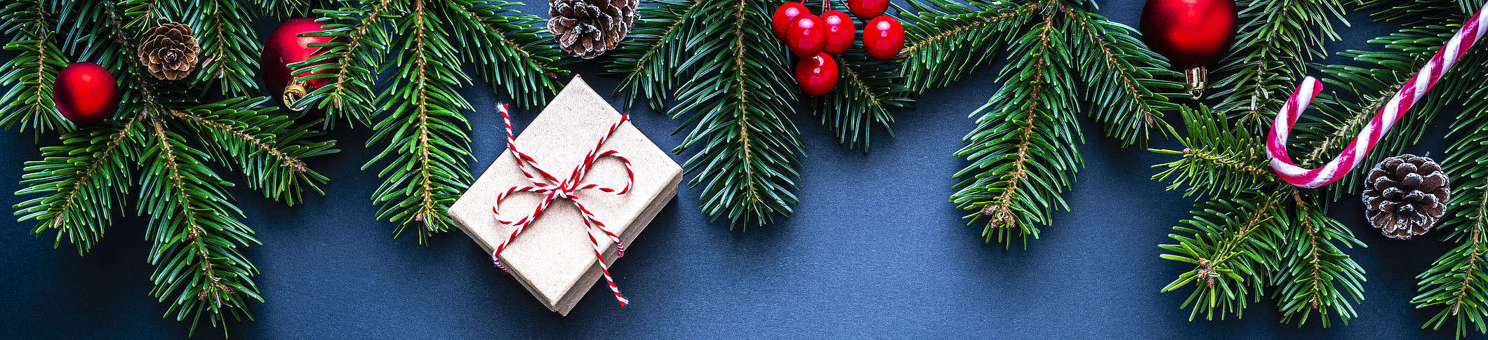 Tannenzweige mit roten Beeren, Zapfen, Geschenk mit rotem Band und Zuckerstange auf blauem Hintergrund