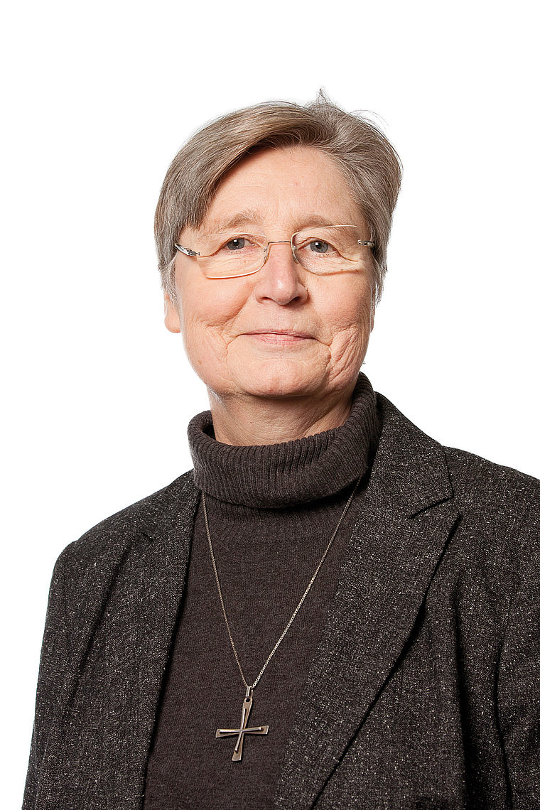 Porträt von Schwester Scholastika, ältere Frau mit kurzen grauen Haaren, Brille, dunklem Rollkragenpullover und Kreuzkette