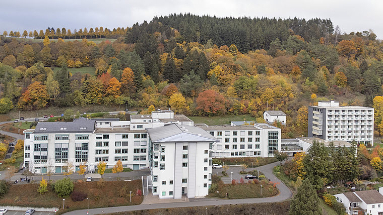 Mehrere weiße Gebäude vor einem bewaldeten Hügel mit herbstlich gefärbtem Laub