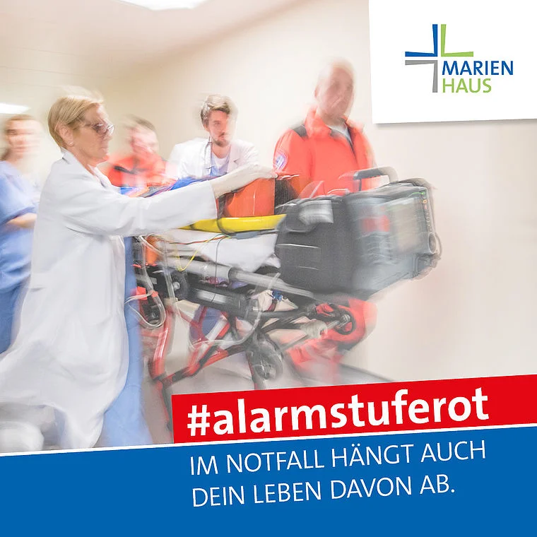 Medizinisches Personal transportiert einen Patienten auf einer Trage im Krankenhaus Marienhaus, Text '#alarmstuferot Im Notfall hängt auch dein Leben davon ab'