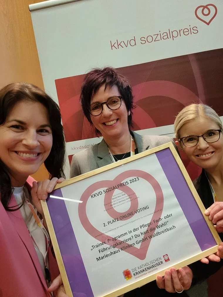 Drei Frauen halten eine Urkunde für den 1. Platz des kkvd Sozialpreises 2023, lächelnd vor einem Banner mit dem kkvd Sozialpreis-Logo