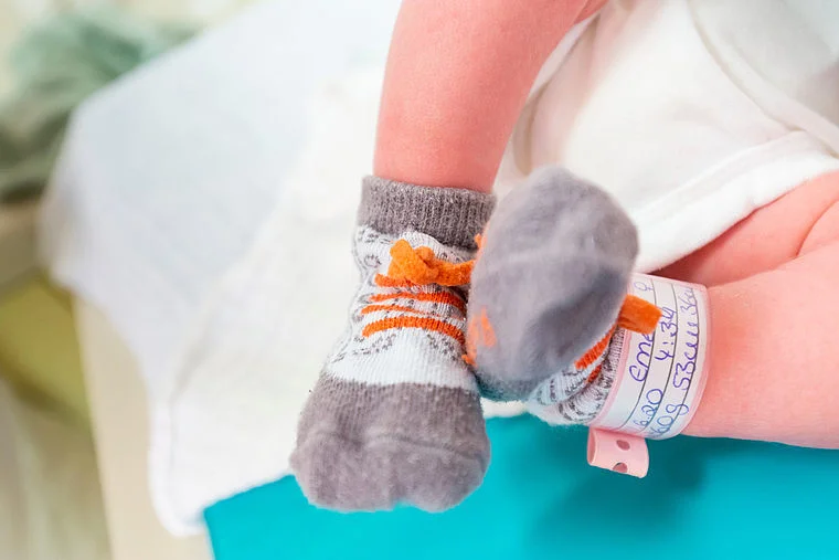 Neugeborenes Baby mit grauen Socken und Krankenhausarmband am Bein